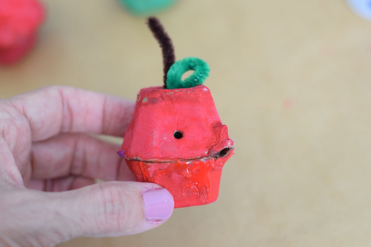 holding an apple egg carton craft with worm hole for pipe cleaner worm to go into