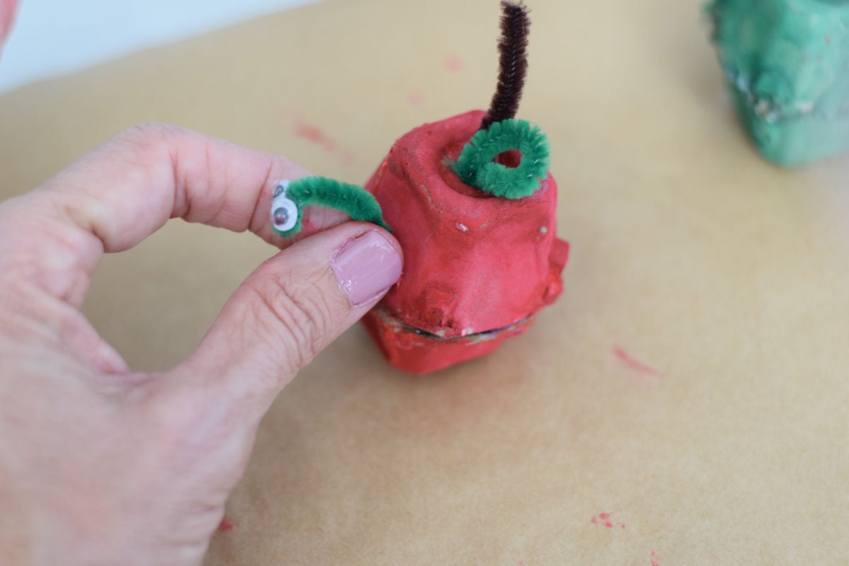 adding a pipe cleaner worm to an apple egg carton craft for kids 