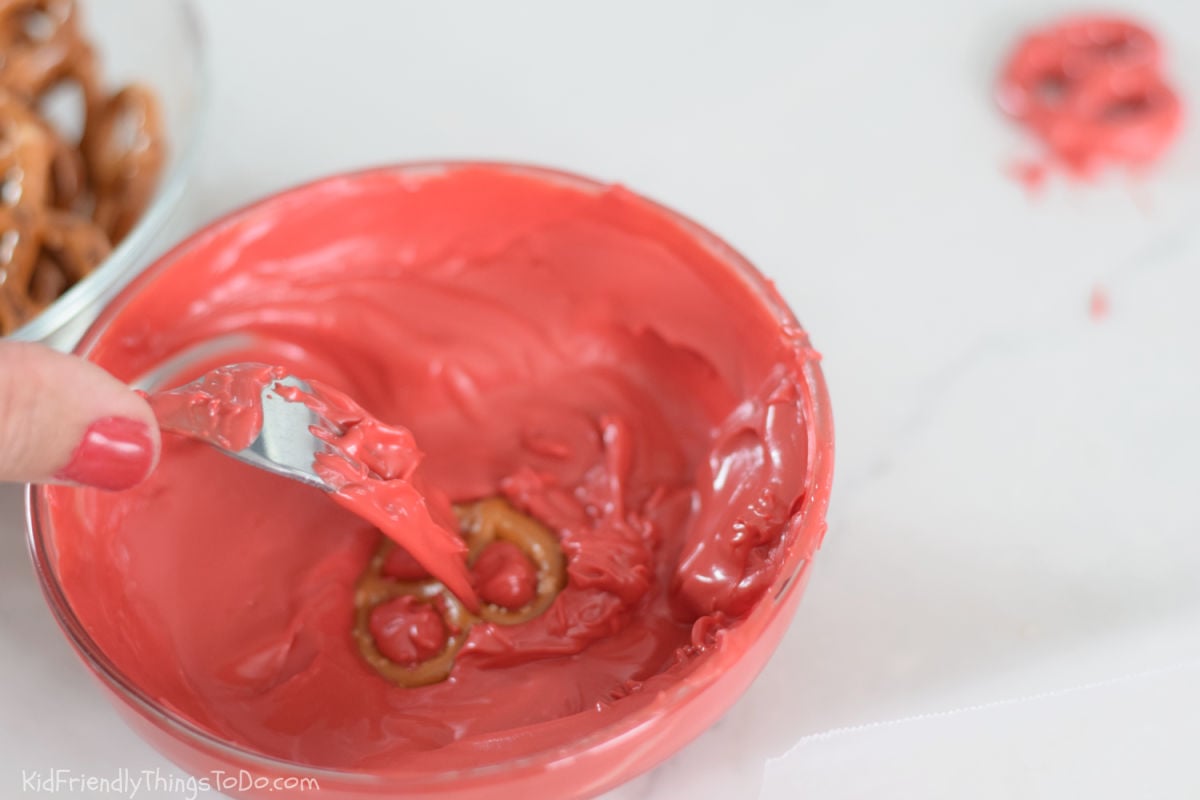 coating mini pretzel twists with red chocolate for chocolate dipped pretzel apples 