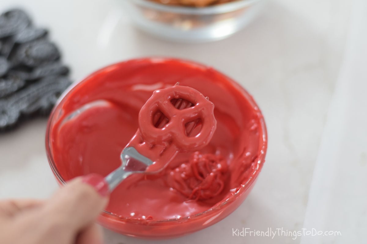 tapping excess chocolate off of mini pretzel twist for chocolate dipped pretzel apples 