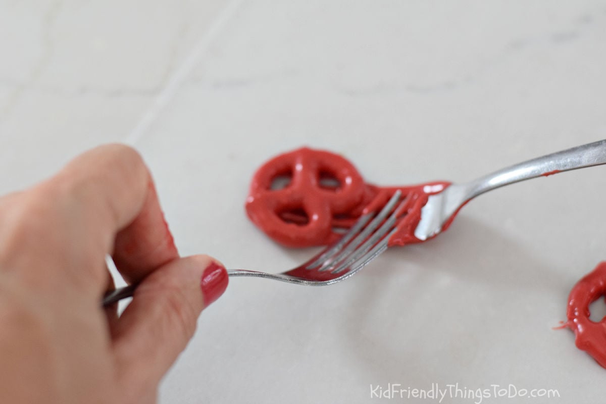 scraping chocolate dipped pretzel off of fork onto wax paper 