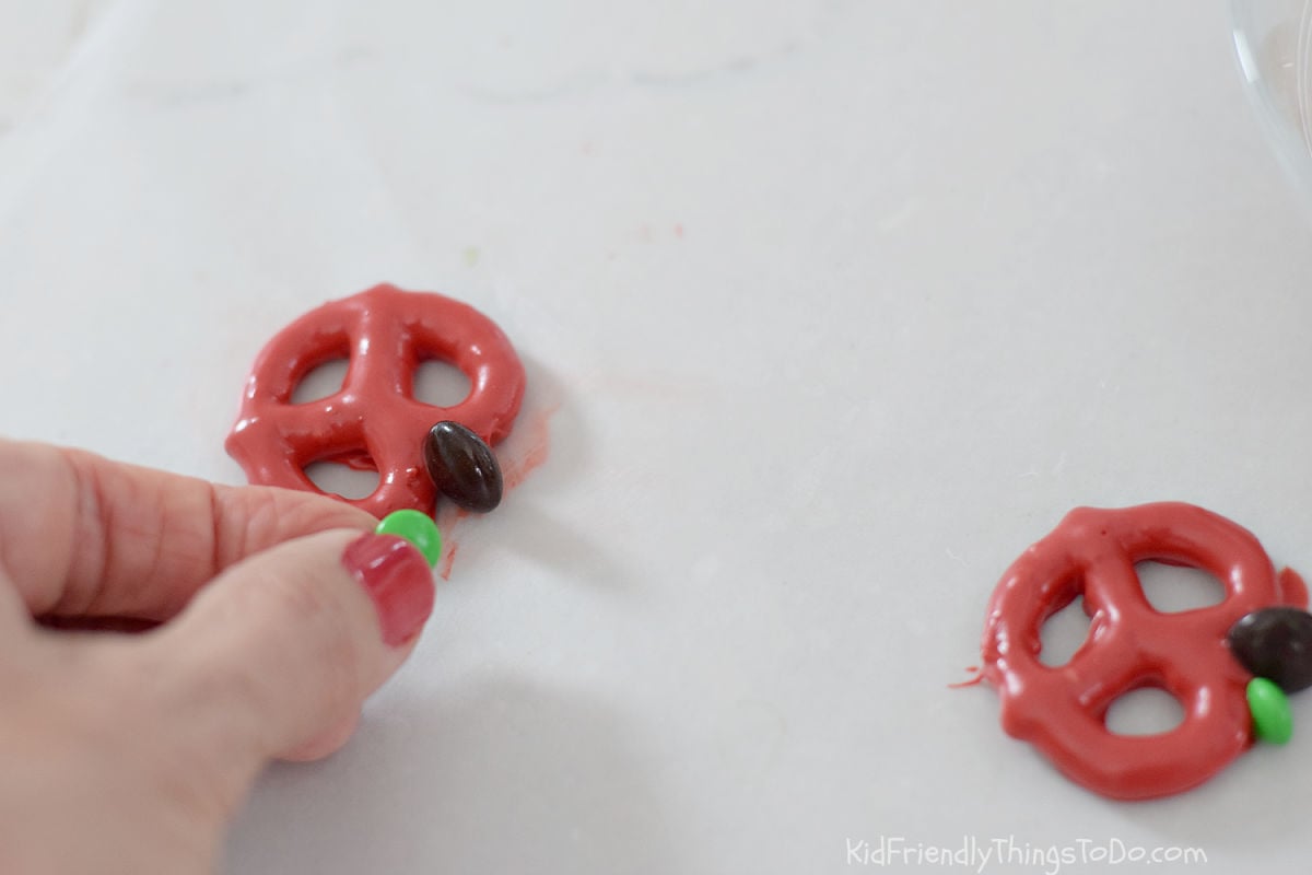 adding M&M stem and leaf to chocolate dipped apple pretzels 