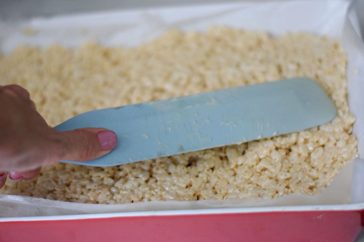 Rice Krispie Treat mixture being spread into a lined baking pan