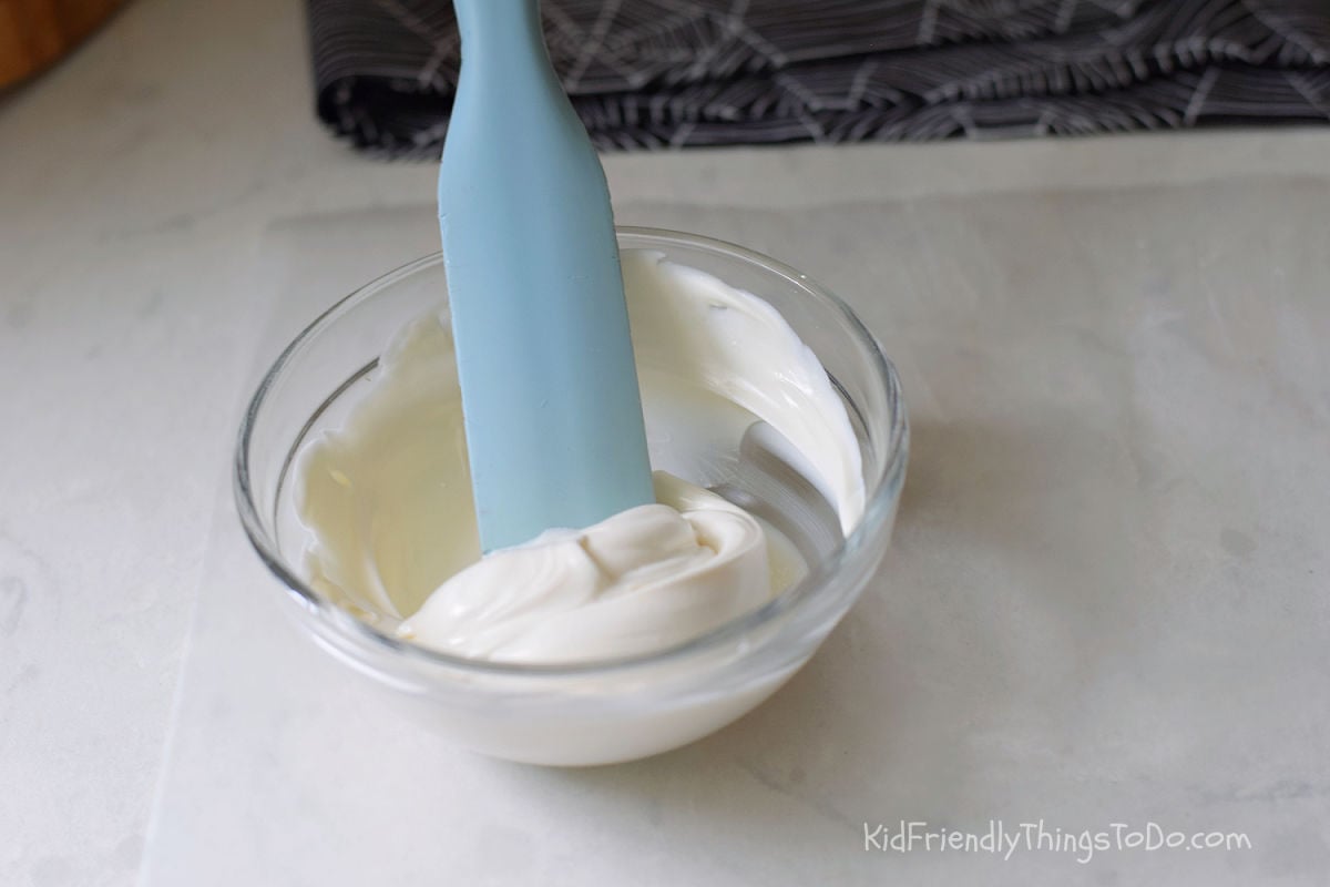 Melted bright white chocolate in a glass bowl with a silicone utensil