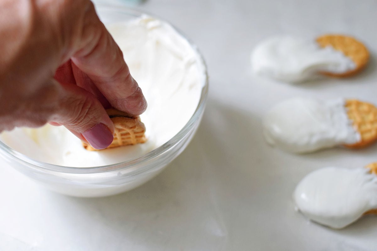 Dipping a Nutter Butter cookie into melted white chocolate to make a ghost