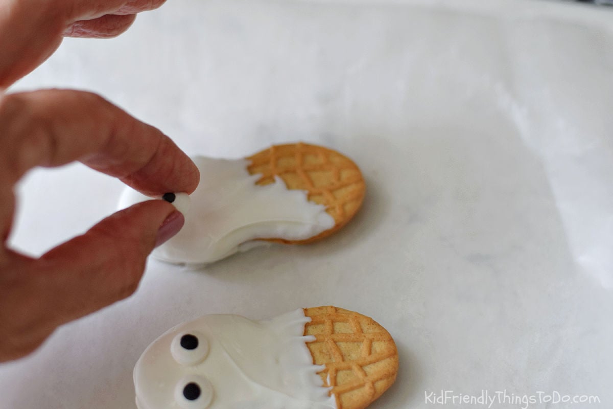 Gently placing a candy eye on a white chocolate-coated Nutter Butter cookie