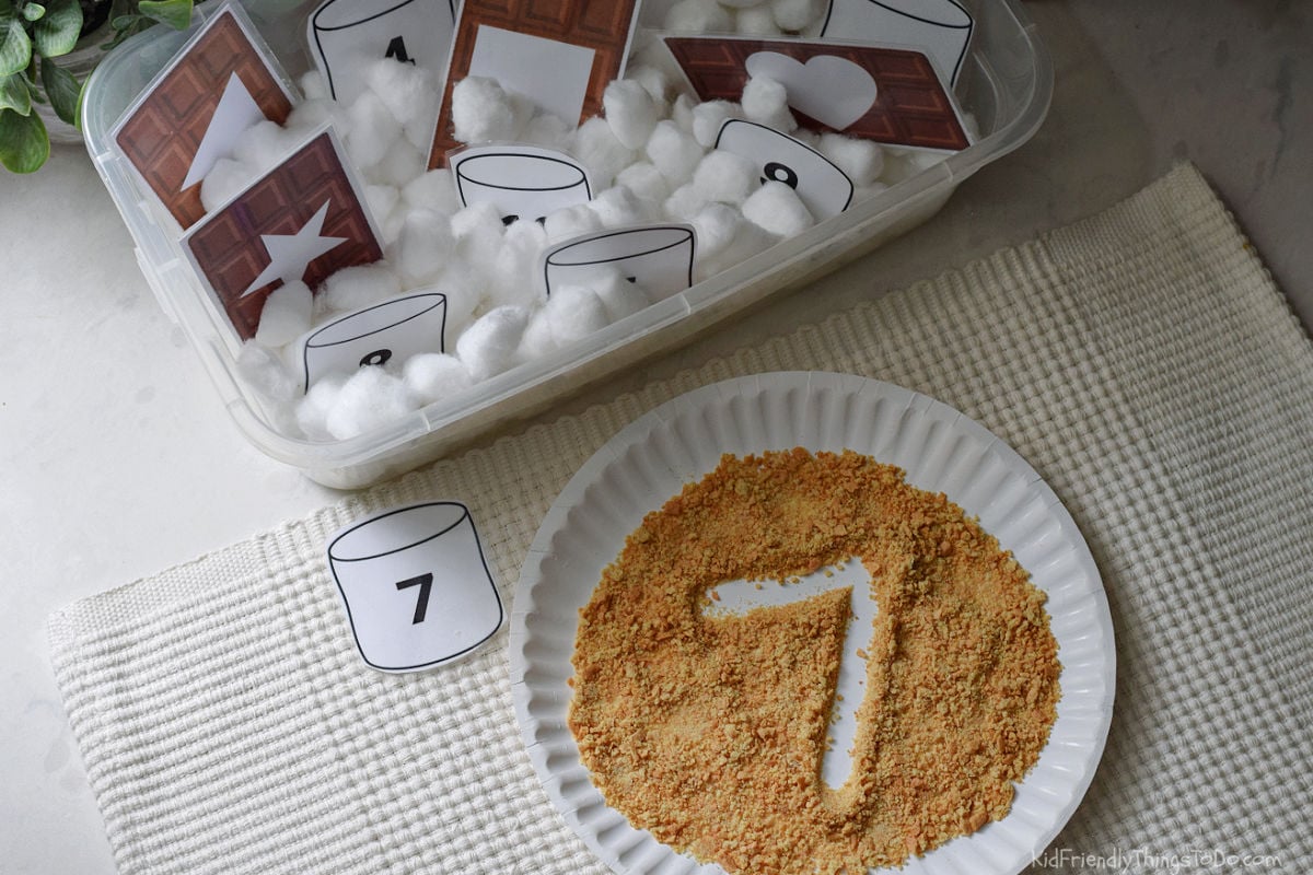 traced number 7 in graham cracker crumbs in front of a S'mores sensory bin for preschoolers