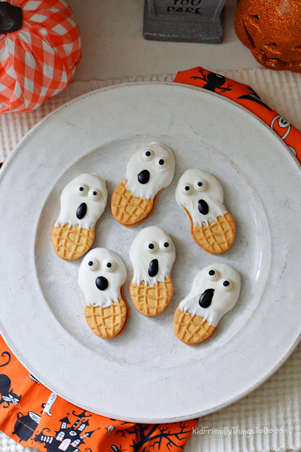 Six Nutter Butter ghosts with white coating, candy eyes, and black oval mouths on a plate