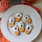Six Nutter Butter ghosts with white coating, candy eyes, and black oval mouths on a plate