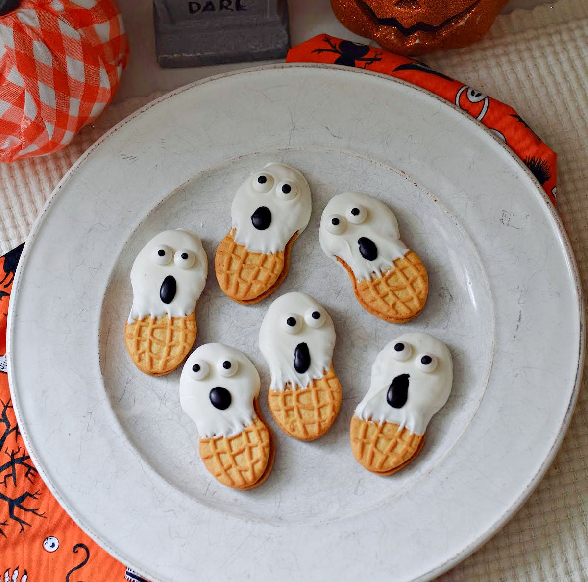 Six Nutter Butter ghosts with white coating, candy eyes, and black oval mouths on a plate
