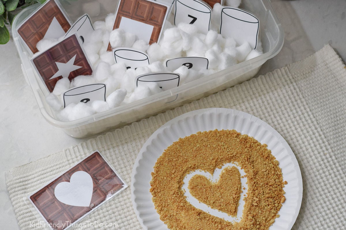 tracing a heart shape in graham crackers from a card pulled from a S'more sensory bin