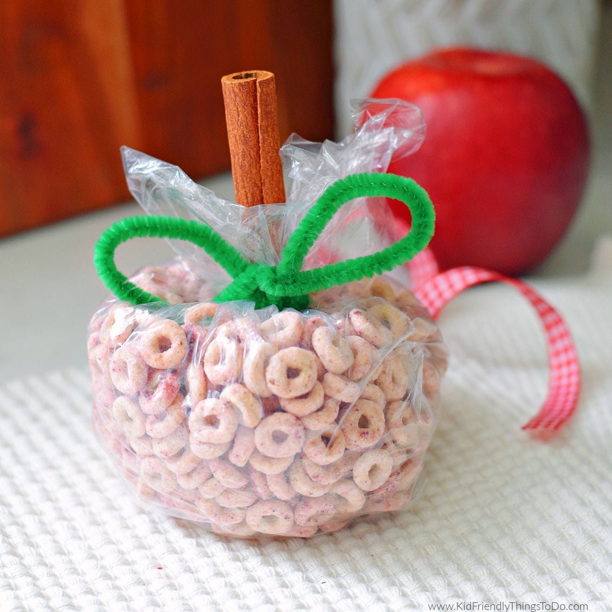 apple Cheerio snack bag shaped into apples with cinnamon stick and pipe cleaner leaves for kids
