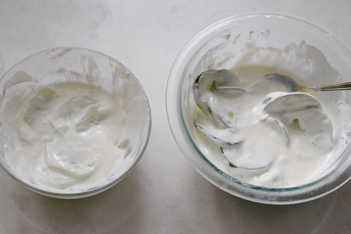 Two glass bowls of creamy cucumber salad, with peeled cucumber slices on the left and skin-on slices on the right.