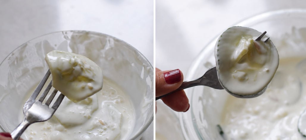 Peeled cucumber slice on the left and unpeeled slice on the right, held on forks and coated in creamy dressing.