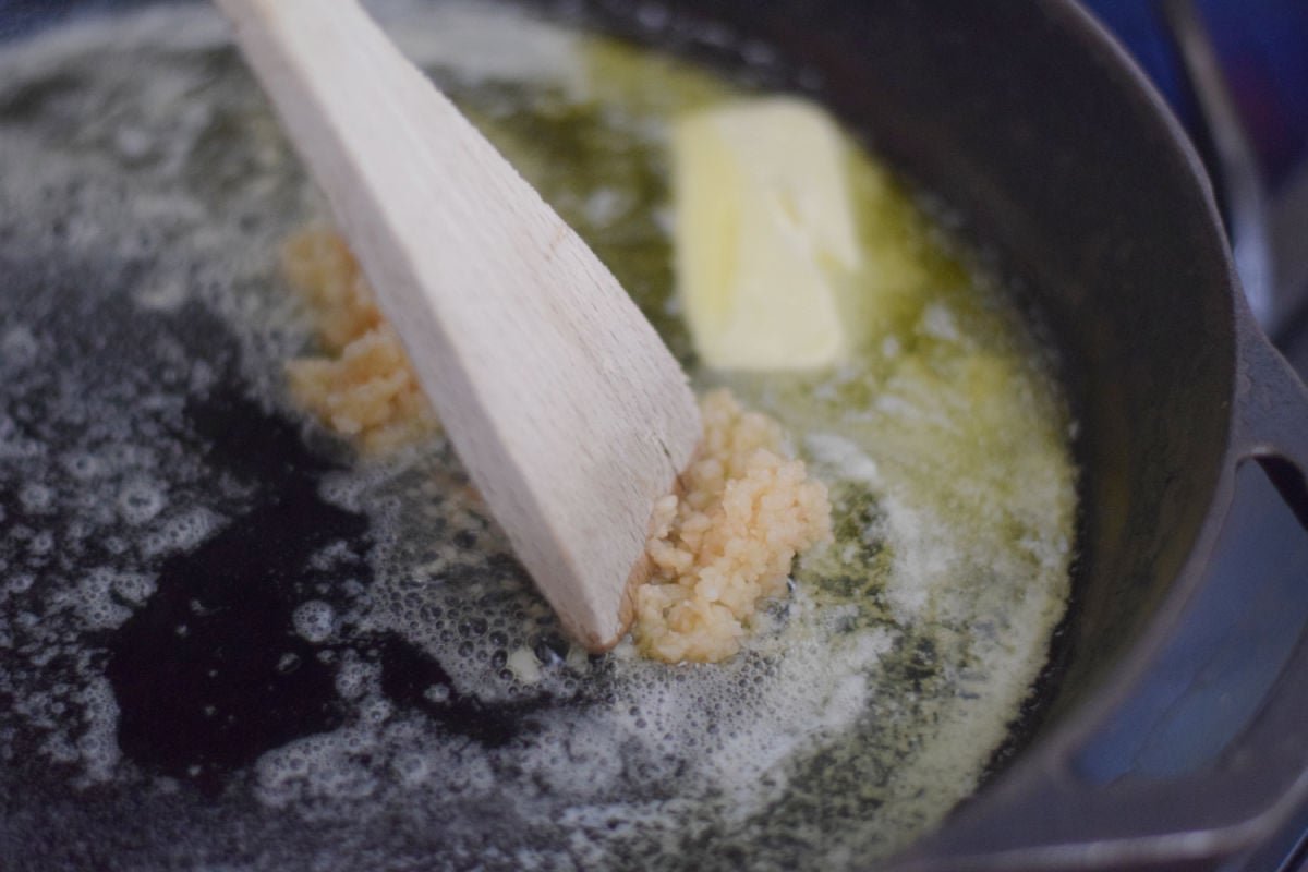 Minced garlic and melting butter in a cast iron skillet with a wooden spoon.