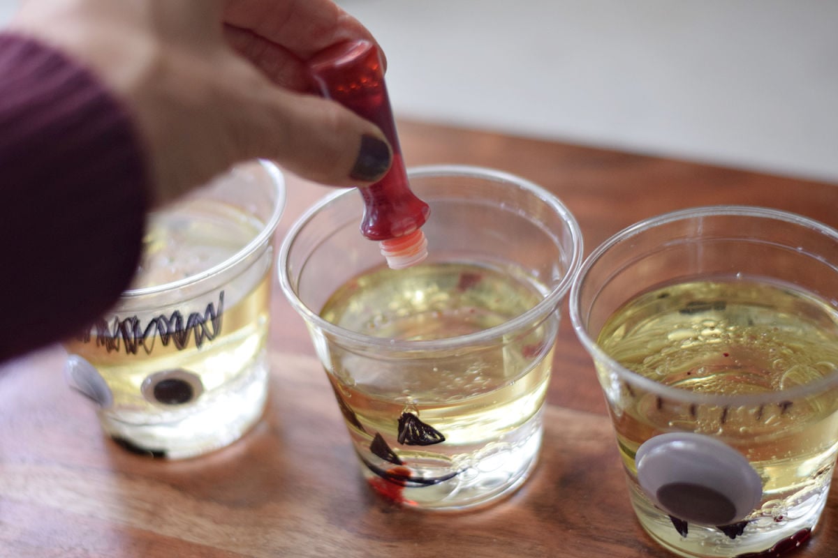 Adding drops of food coloring to oil and water in a jack-o’-lantern cup.