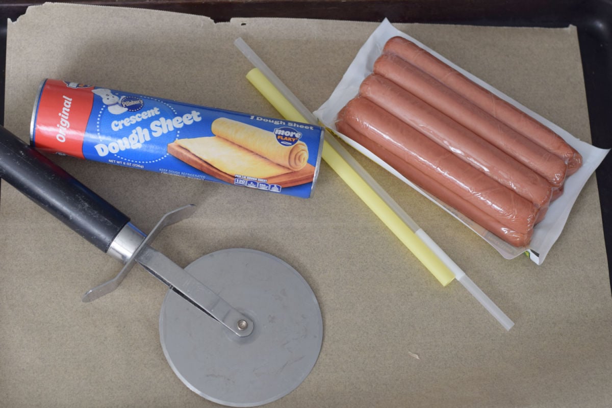Crescent dough sheet, hot dogs, drinking straws, and a pizza cutter for making Ghosts in a Blanket.