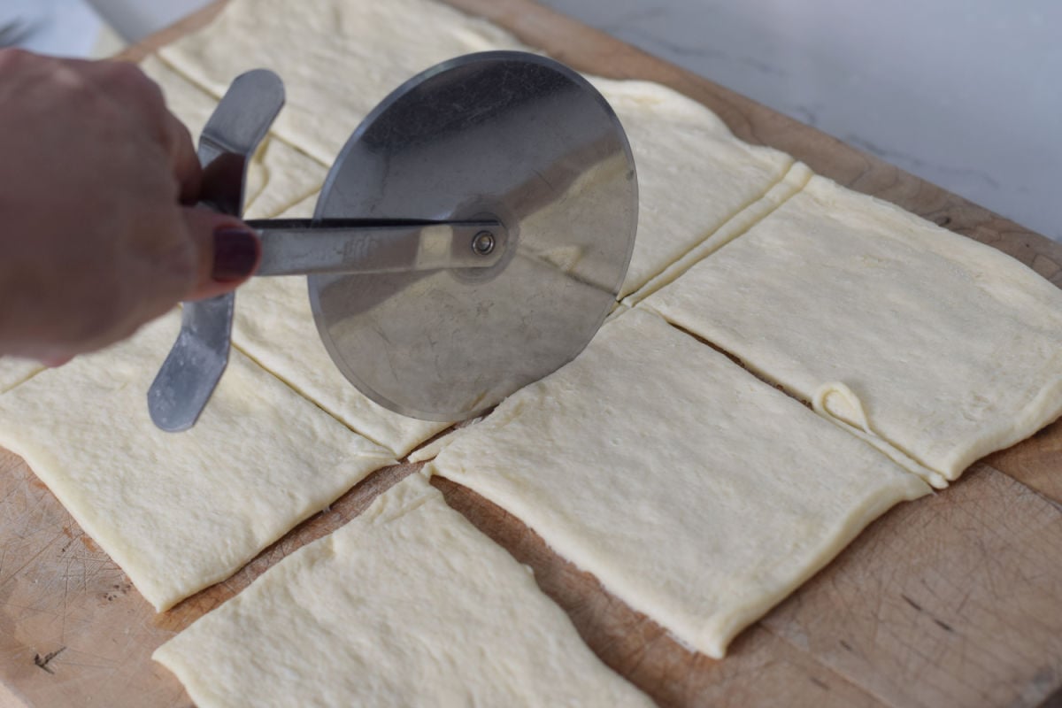  Cutting a crescent dough sheet into rectangles with a pizza cutter.