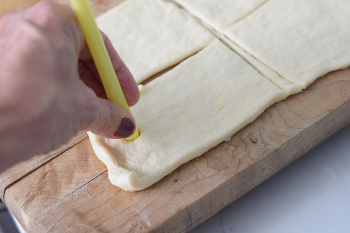 Using a drinking straw to cut a ghost face into a flat rectangle of crescent dough.