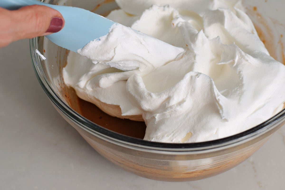 Whipped topping being added to chocolate pudding in a glass mixing bowl.