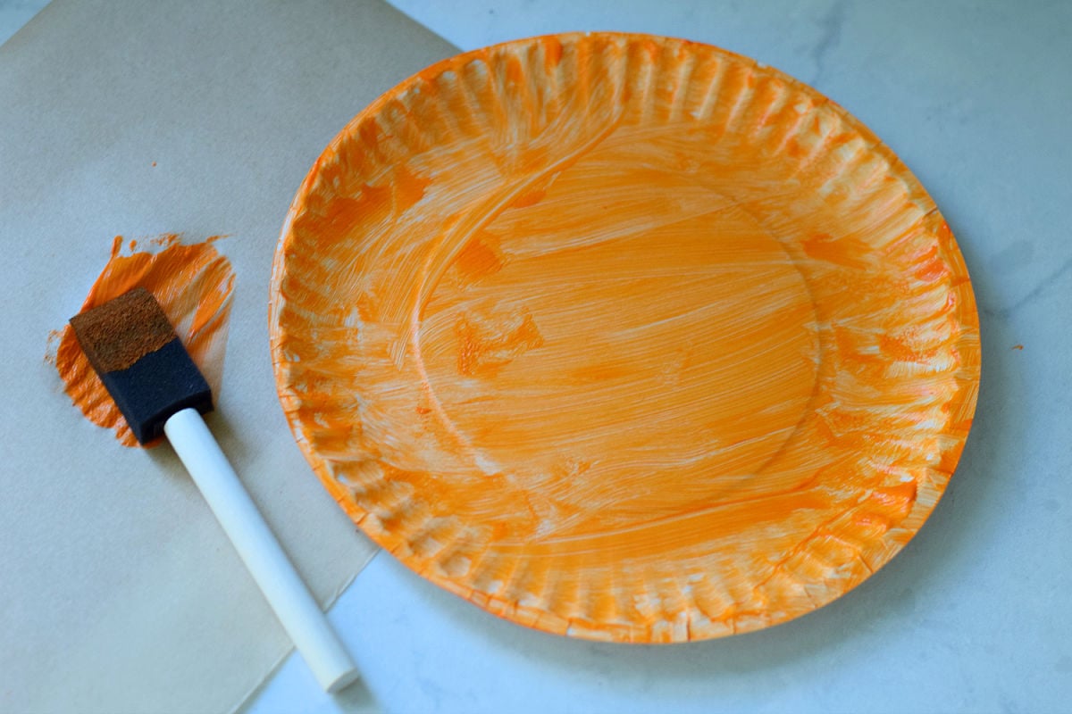 Paper plate painted orange with a foam brush for a Halloween pumpkin craft.