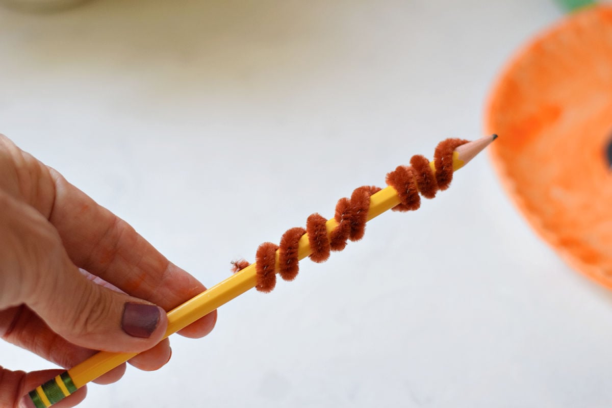 Brown pipe cleaner wrapped around a pencil to make a curly vine for a paper plate pumpkin.