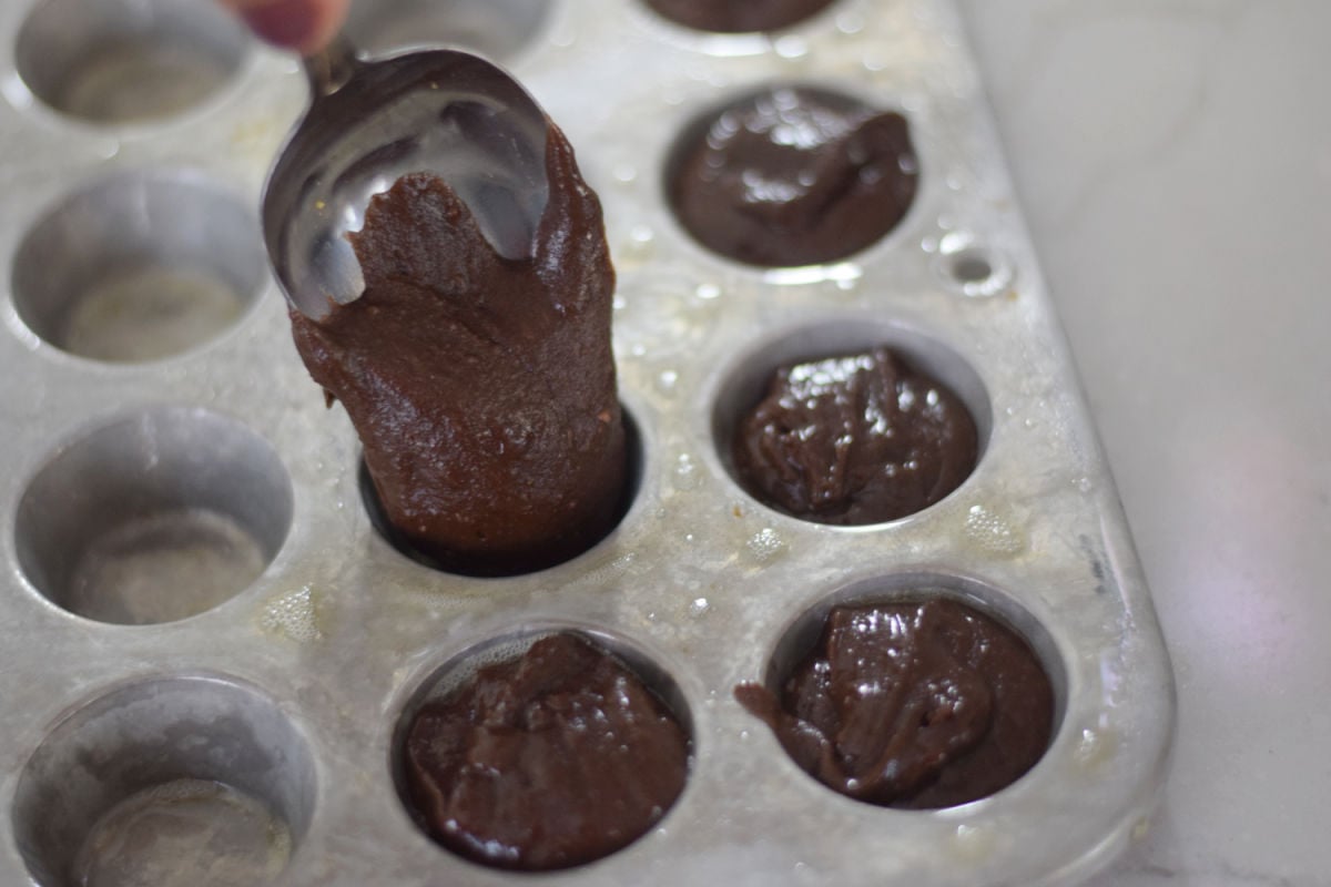 Spooning brownie batter into generously greased mini muffin cups, filling each level with the top.