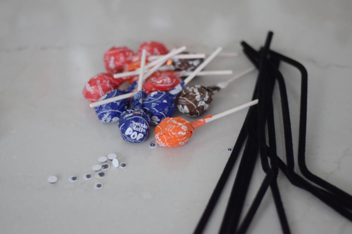 Wrapped Tootsie Pops, black pipe cleaners, and googly eyes for a spider lollipop craft.