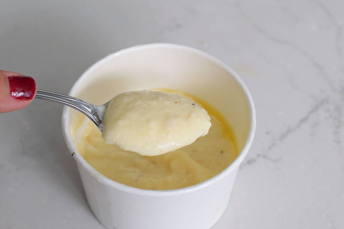 Spoonful of Olive Garden Alfredo sauce held above its takeout container.