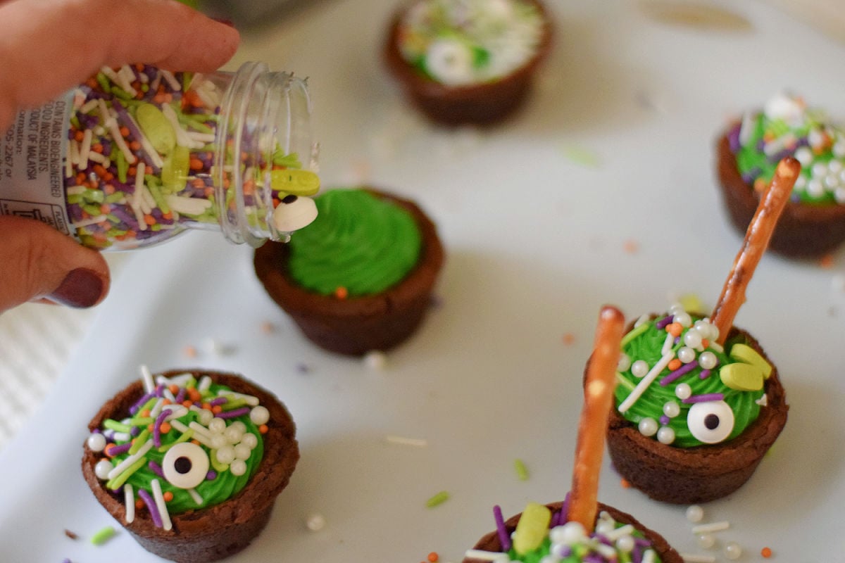 Adding Monster Lab sprinkles and white candy bubbles to green-frosted brownie cauldrons.
