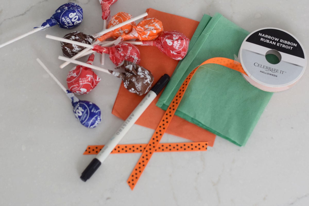 Wrapped Tootsie Pops, orange and green tissue paper, orange ribbon, and a black paint marker for making pumpkin lollipops.