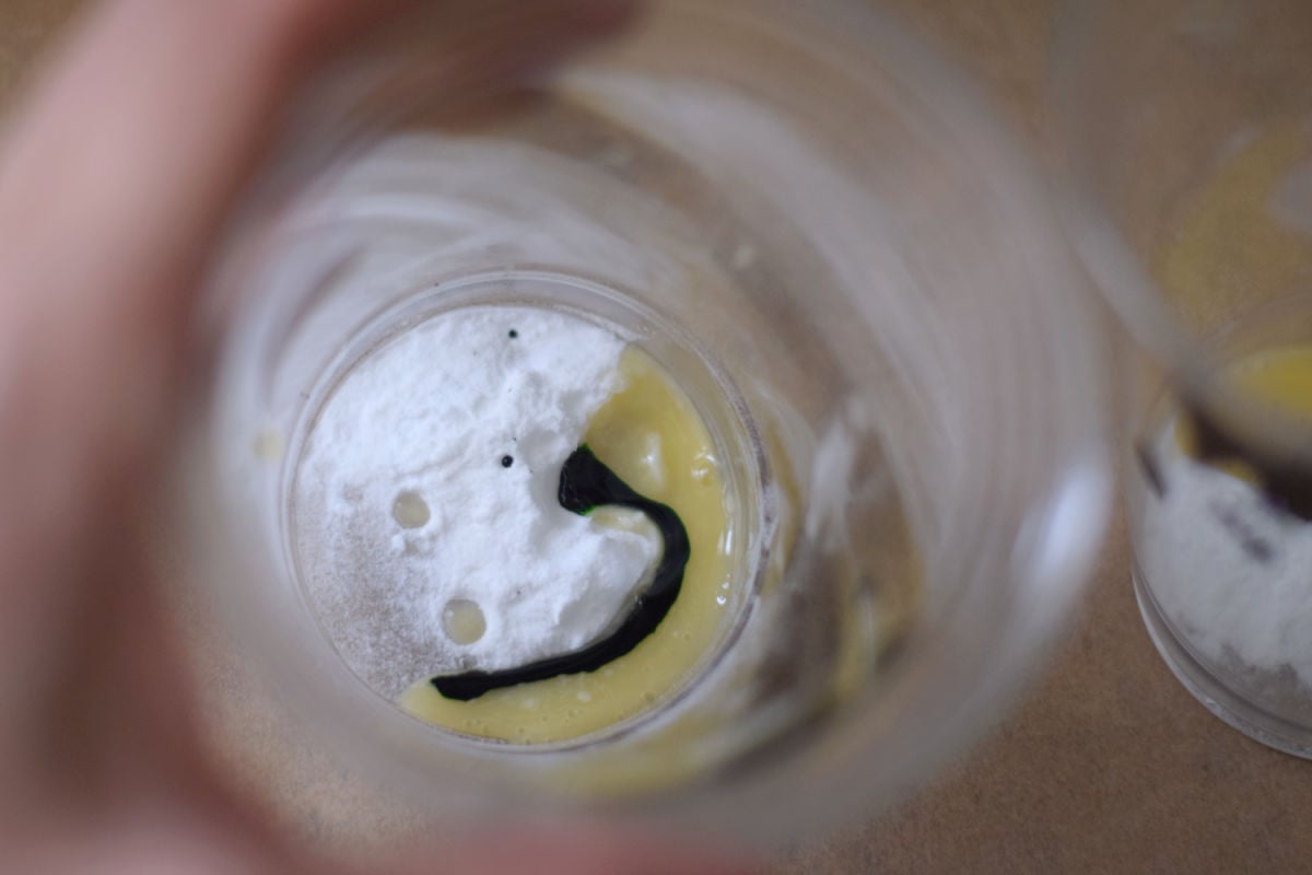Baking soda, liquid egg whites, and drops of green food coloring inside a clear Frankenstein cup.