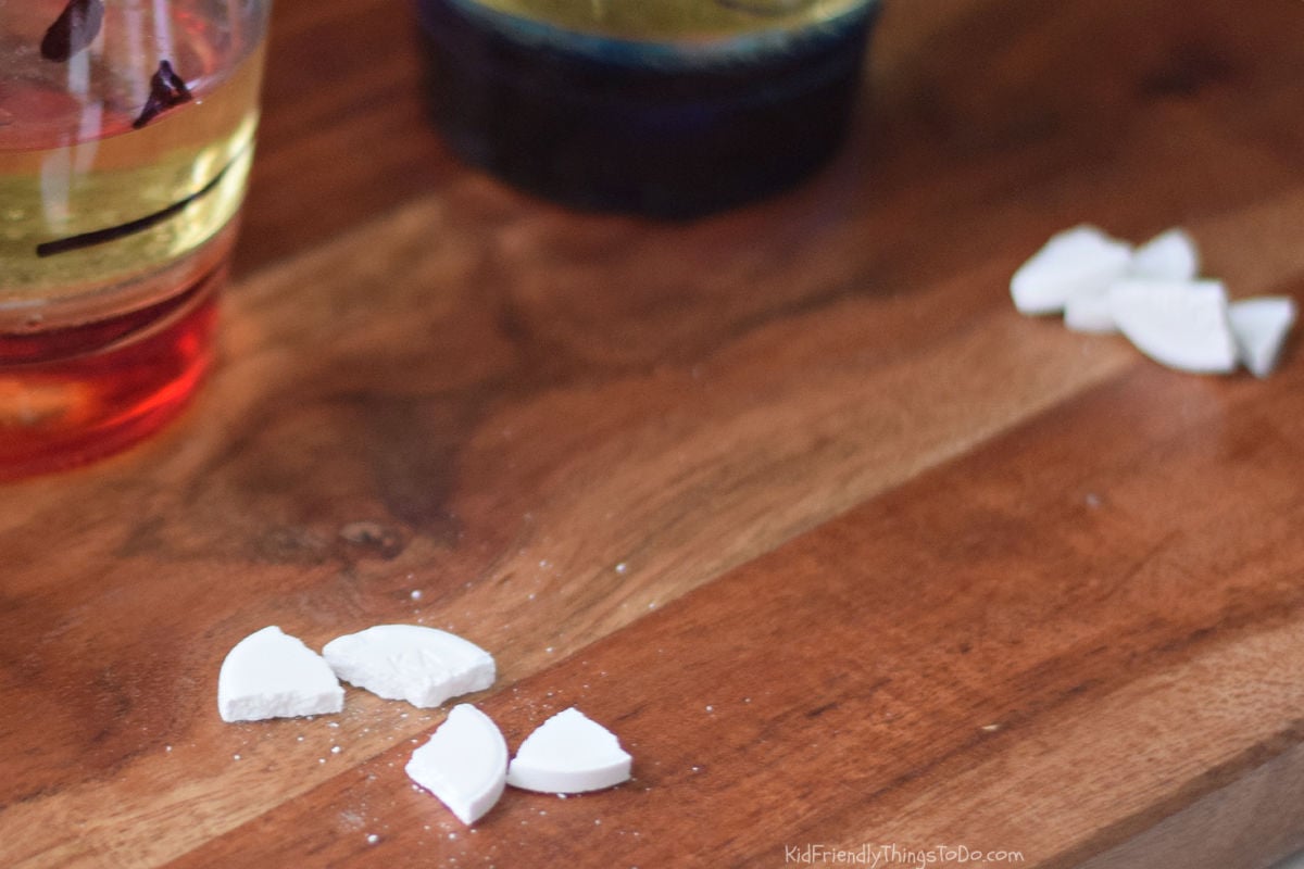 Alka-Seltzer tablet broken into four pieces on a wooden board.