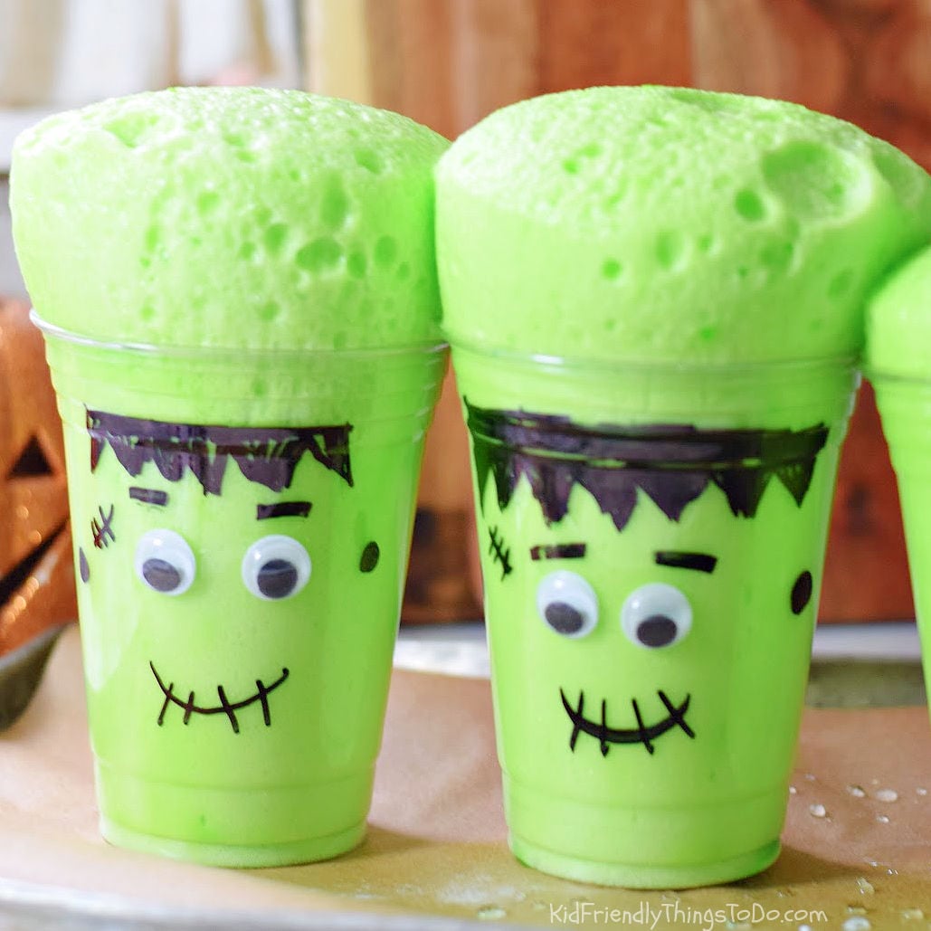 Two Frankenstein cups with thick green foam rising above their rims, showing bubbles across the surface.