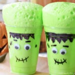 Two Frankenstein cups with thick green foam rising above their rims, showing bubbles across the surface.