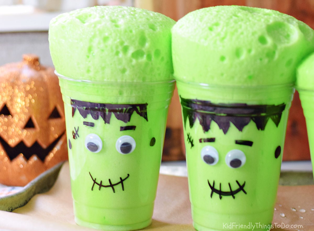 Two Frankenstein cups with thick green foam rising above their rims, showing bubbles across the surface.