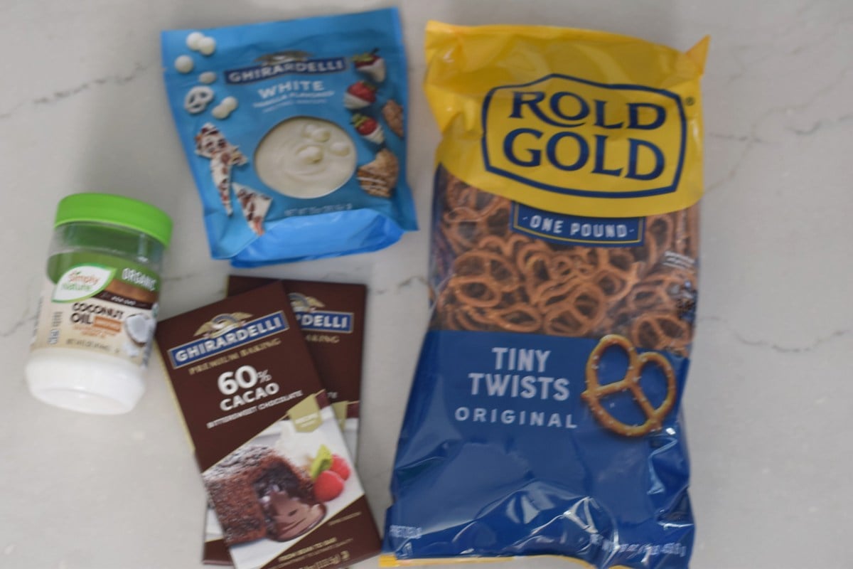 Pretzel twists, Ghirardelli dark chocolate baking bars, white candy melts, and coconut oil on a counter.