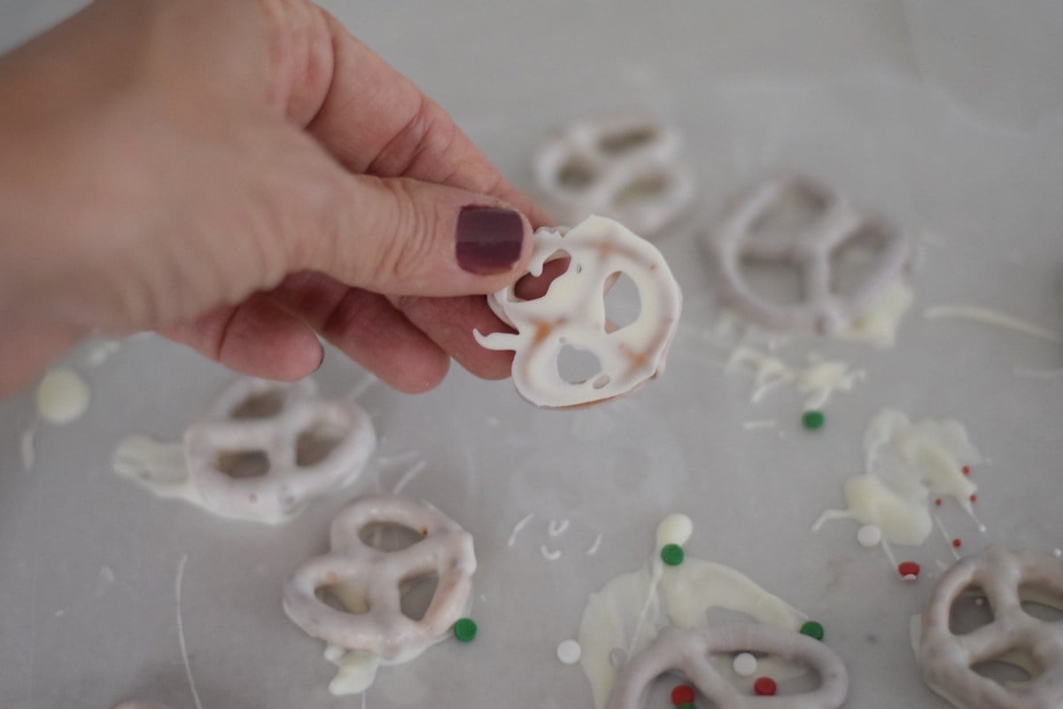 Lifting a set white-coated pretzel from the paper-lined tray.