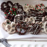 Chocolate covered pretzel twists with dark and white chocolate drizzle, red, green, and white sprinkles on a white platter.
