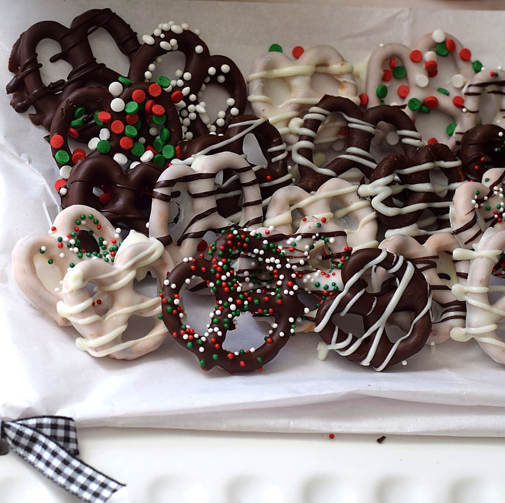Chocolate covered pretzel twists with dark and white chocolate drizzle, red, green, and white sprinkles on a white platter.