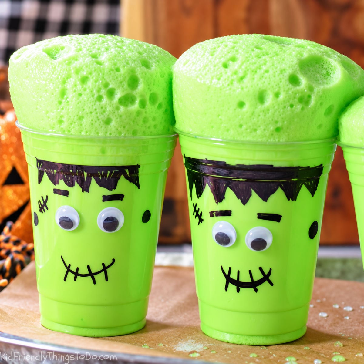 Two Frankenstein cups with thick green foam rising above their rims, showing bubbles across the surface.