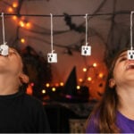 Players trying to eat marshmallow ghosts hanging from strings during a Halloween party game.