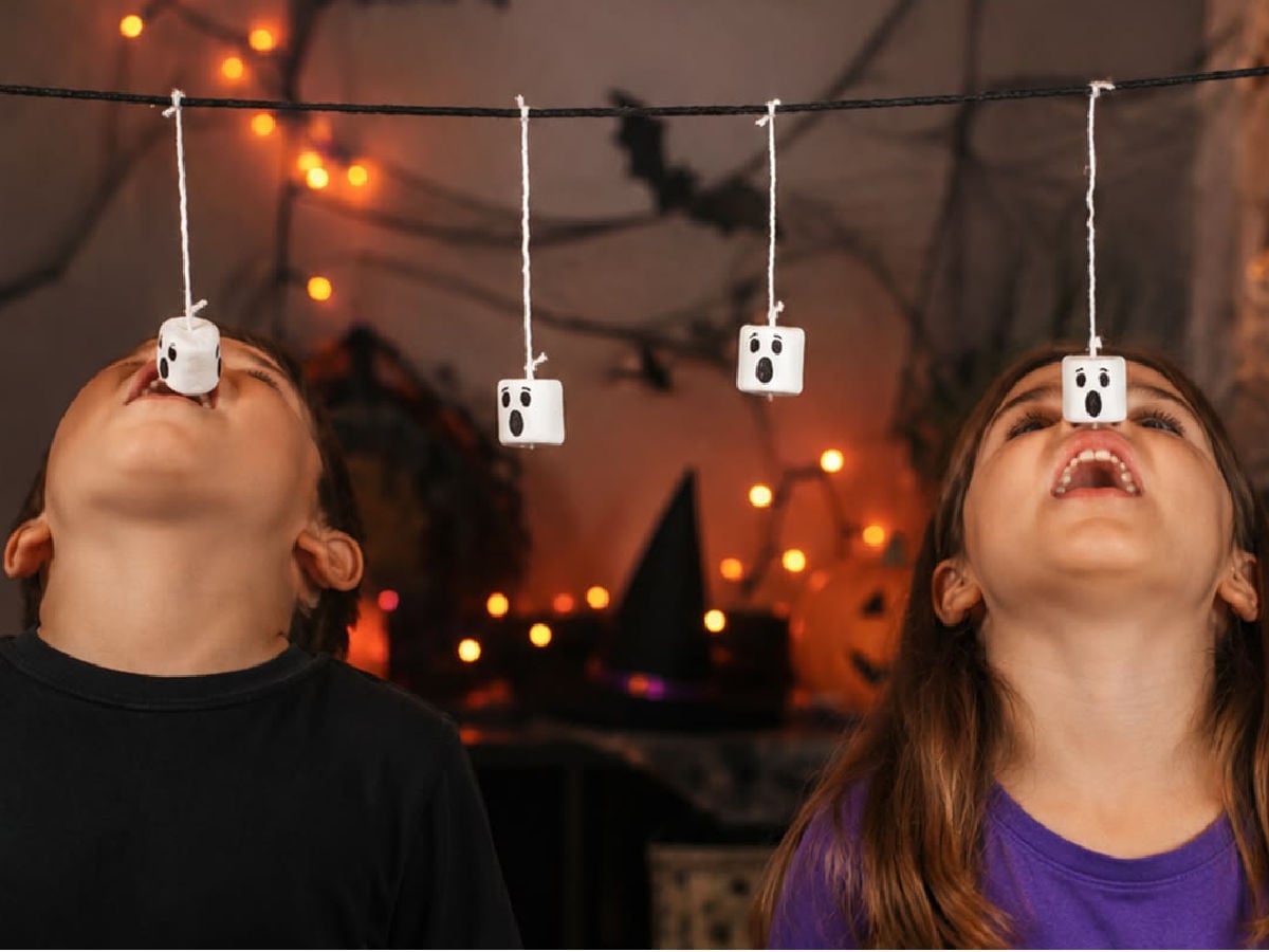 Players trying to eat marshmallow ghosts hanging from strings during a Halloween party game.