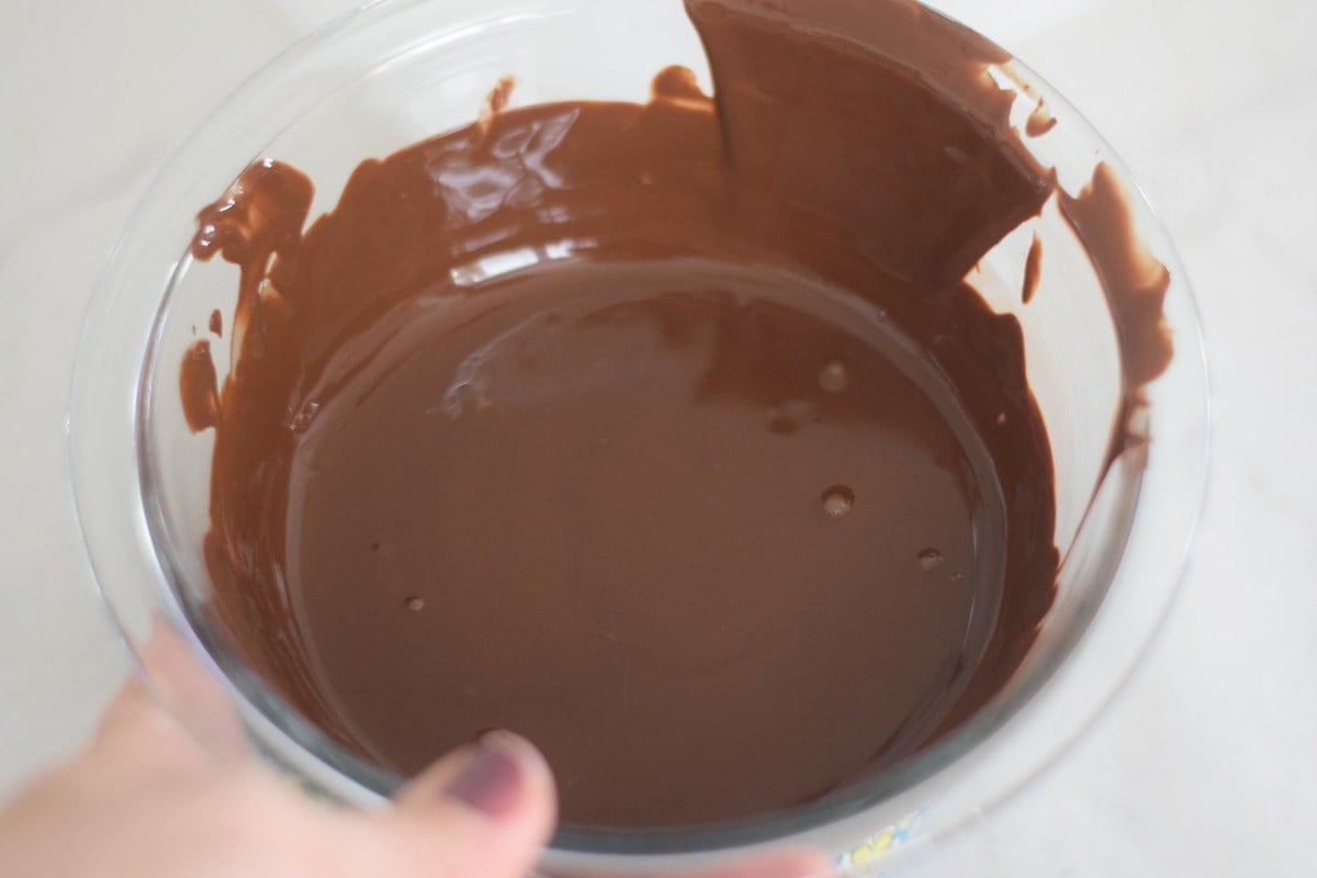Smooth melted dark chocolate in a small glass bowl for dipping pretzels.