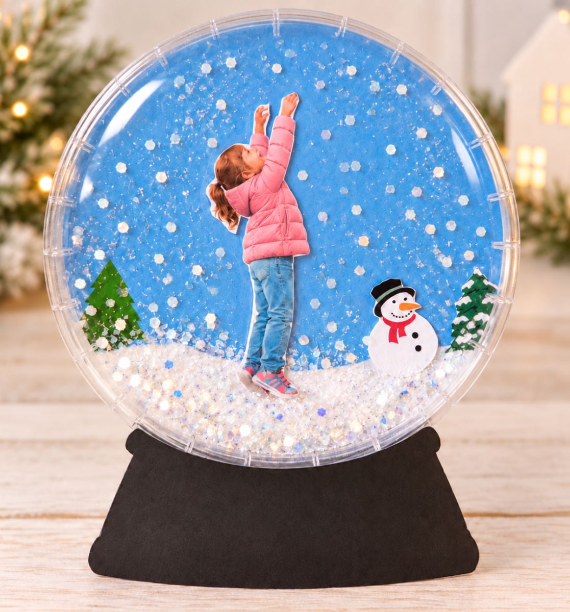 Snow globe bulletin board craft with a child's photo, snowy background, evergreen tree, and black base